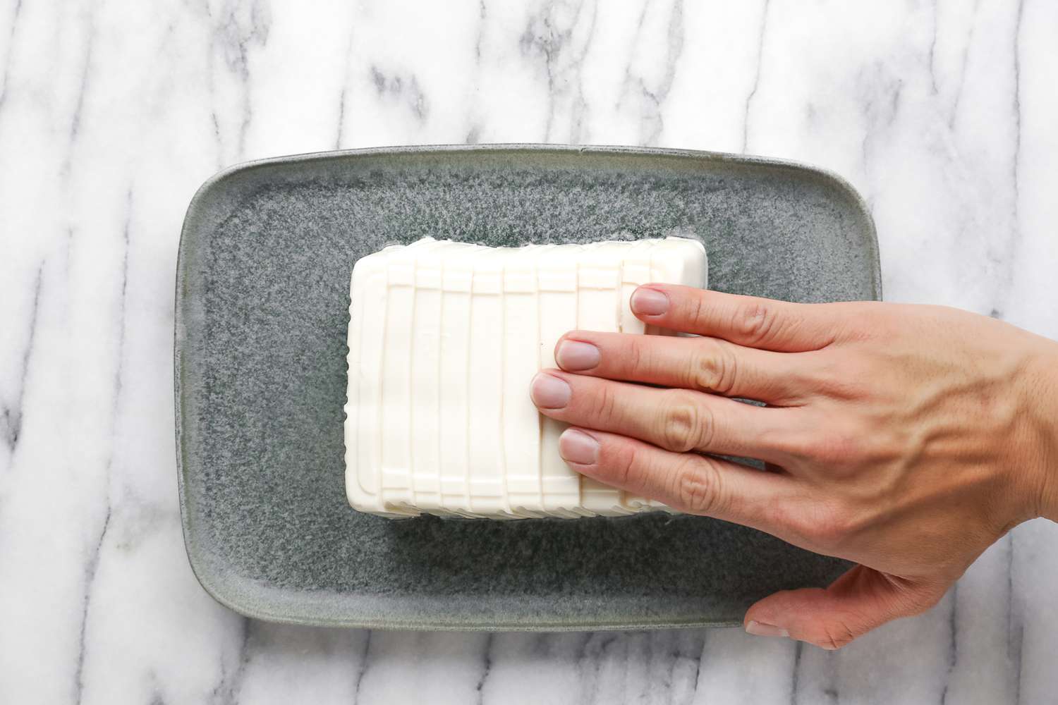 A Hand Gently Pressing Down on Silken Tofu Slabs to Fan It onto the Platter for Sesame Soy Sauce Silken Tofu Recipe