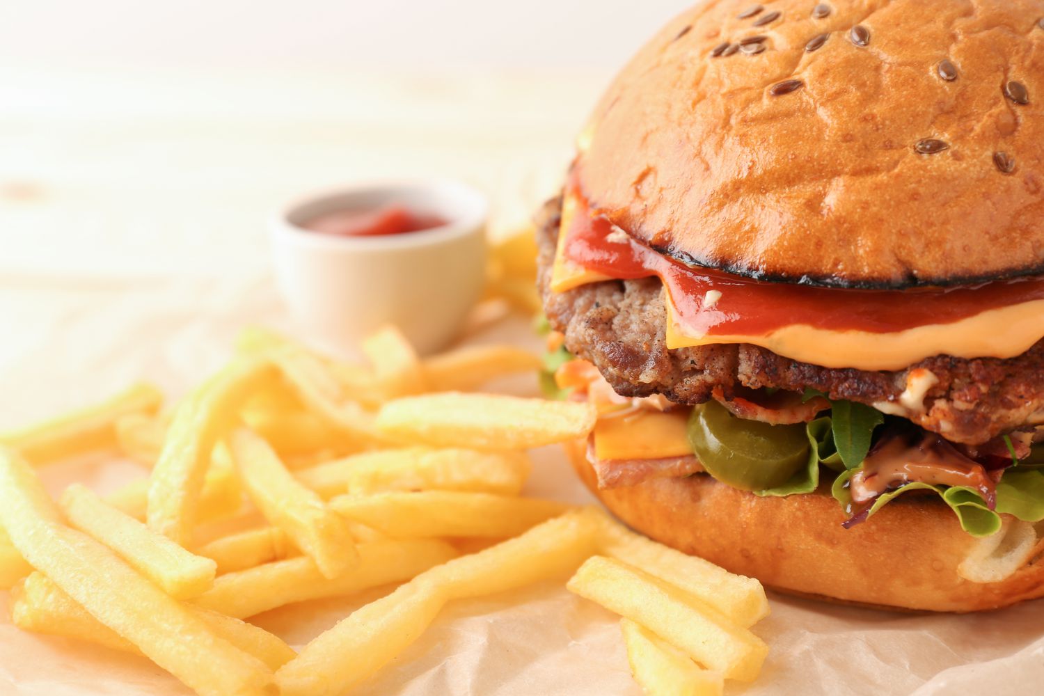 A burger with toppings served with french fries and a small container of ketchup