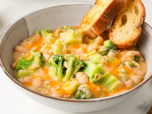 Angled view of a stoneware bowl of Broccoli Cheddar Creamy Beans next to a spoon and all on a white background