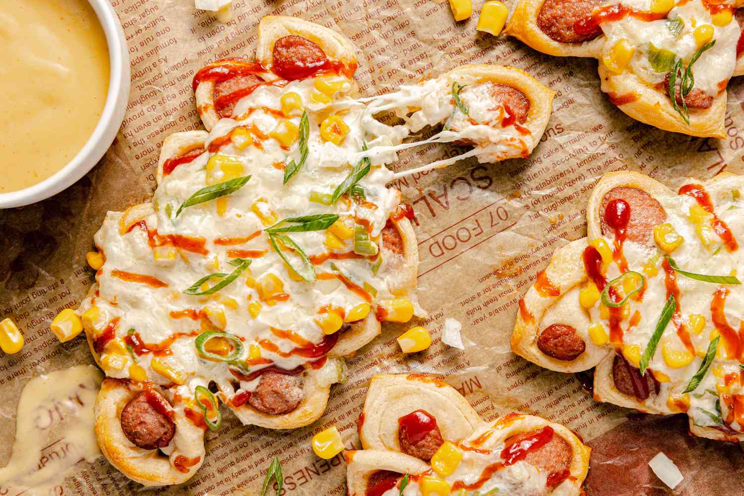 Pull-Apart Corn Cheese Pigs in a Blanket with a Piece Pulled Off, Surrounded by More and a Bowl of Mustard