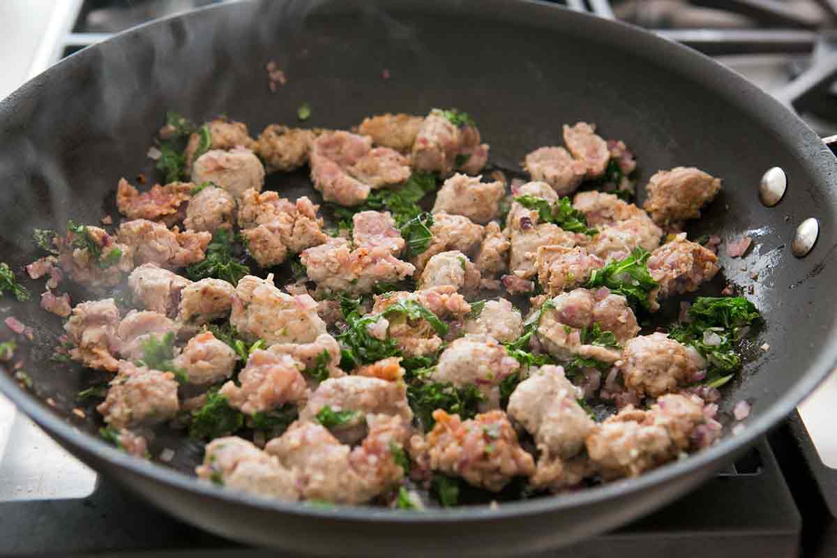 browning sausage in a pan with kale and onion