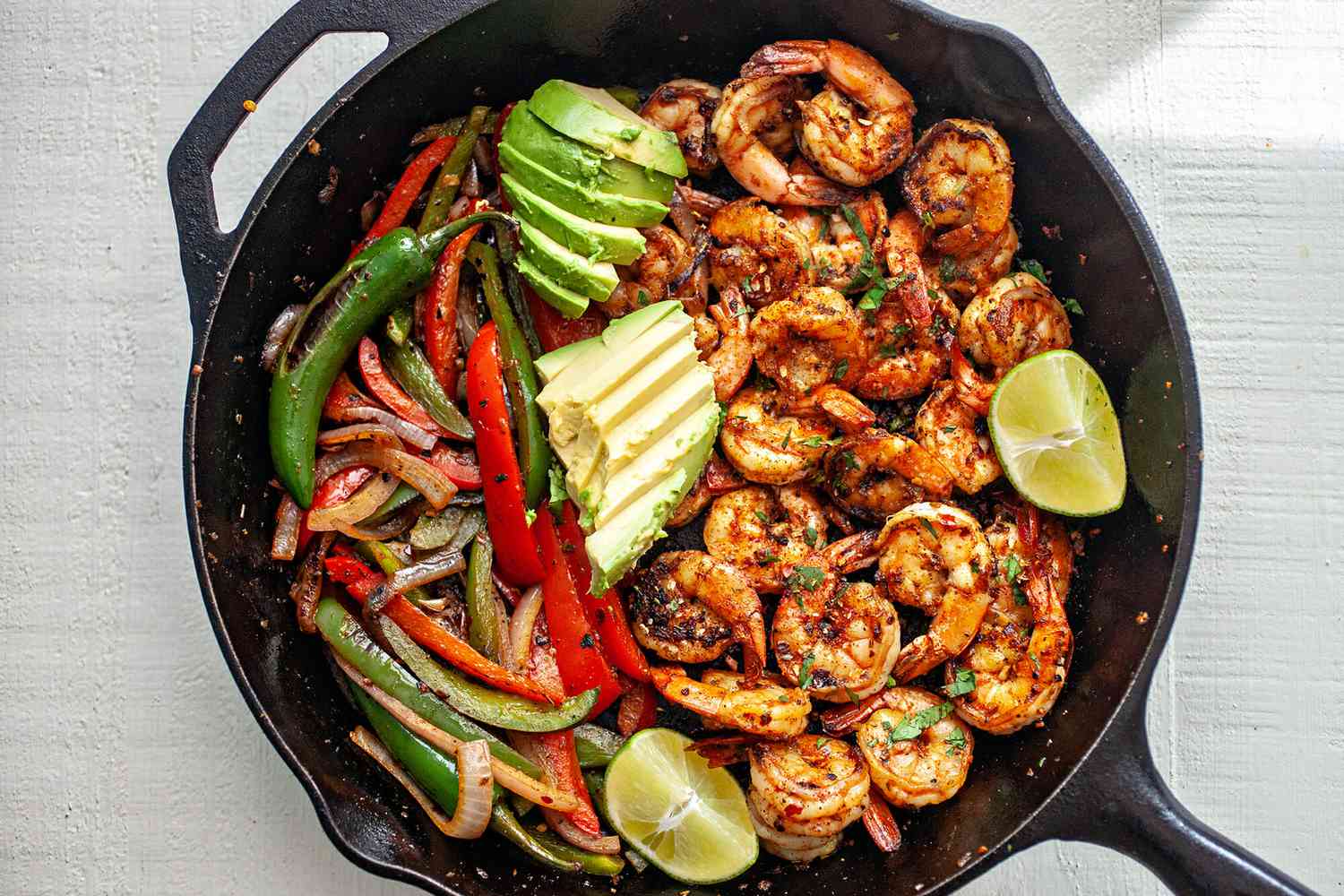 Shrimp Fajitas in a cast iron skillet topped with lime wedges and sliced avocado
