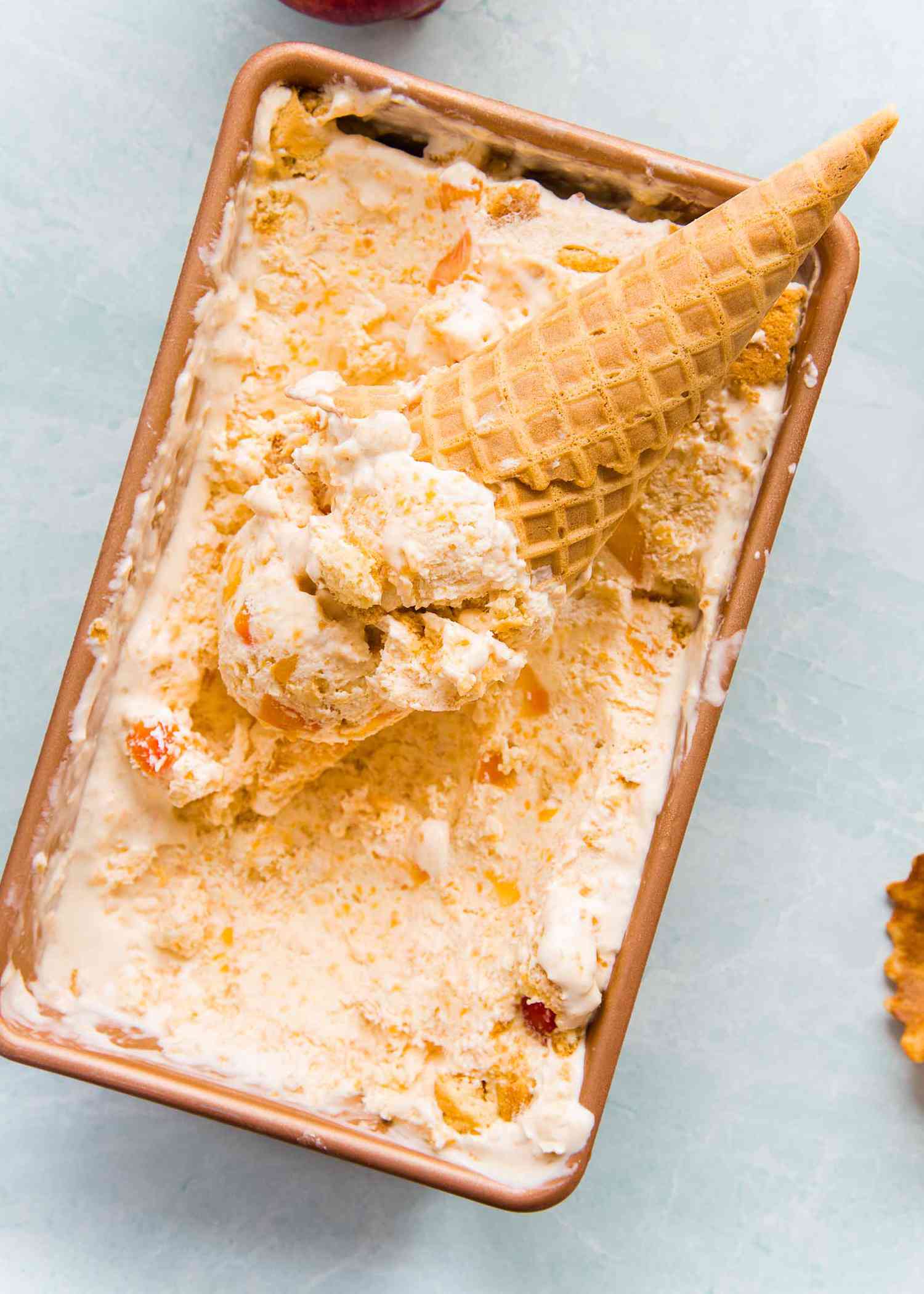 Easy peach cobbler ice cream fills a loaf pan and an ice cream cone is on top.