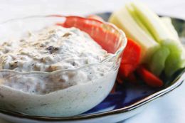 A bowl of crab dip on a platter with veggie sticks