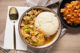 Microwave Oyakodon and Rice in a Small Plate Surrounded by a Table Setting with a Spoon, a Table Napkin, and a Small Plate with Kimchi
