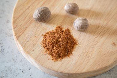 Pile of ground nutmeg next to three whole nutmegs