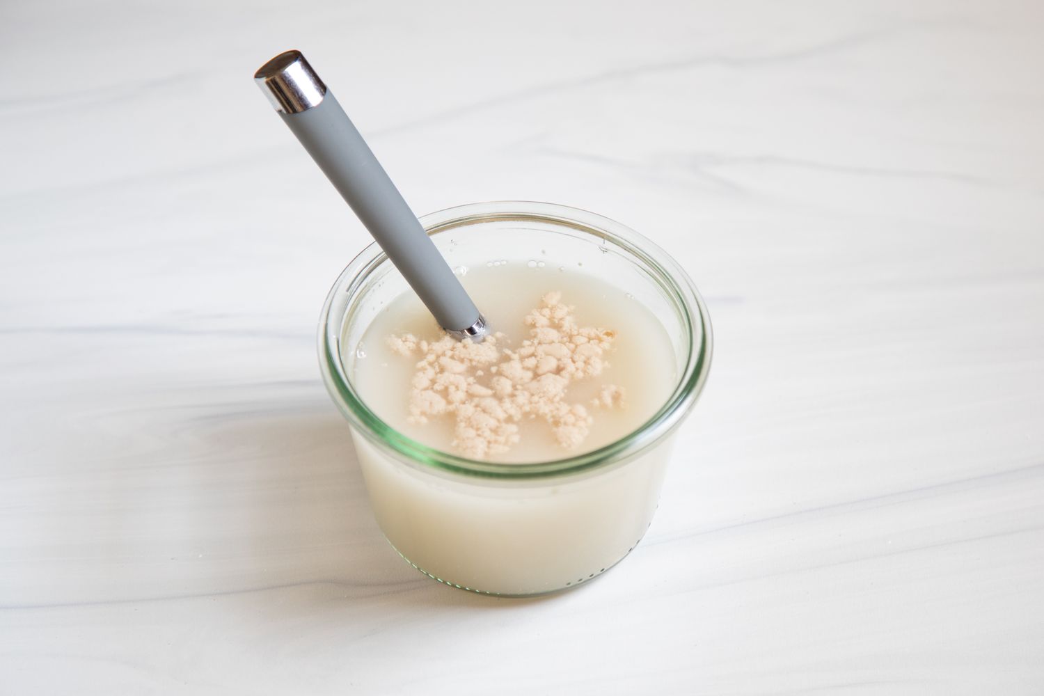 A spoon in a glass cup with water and yeast inside.