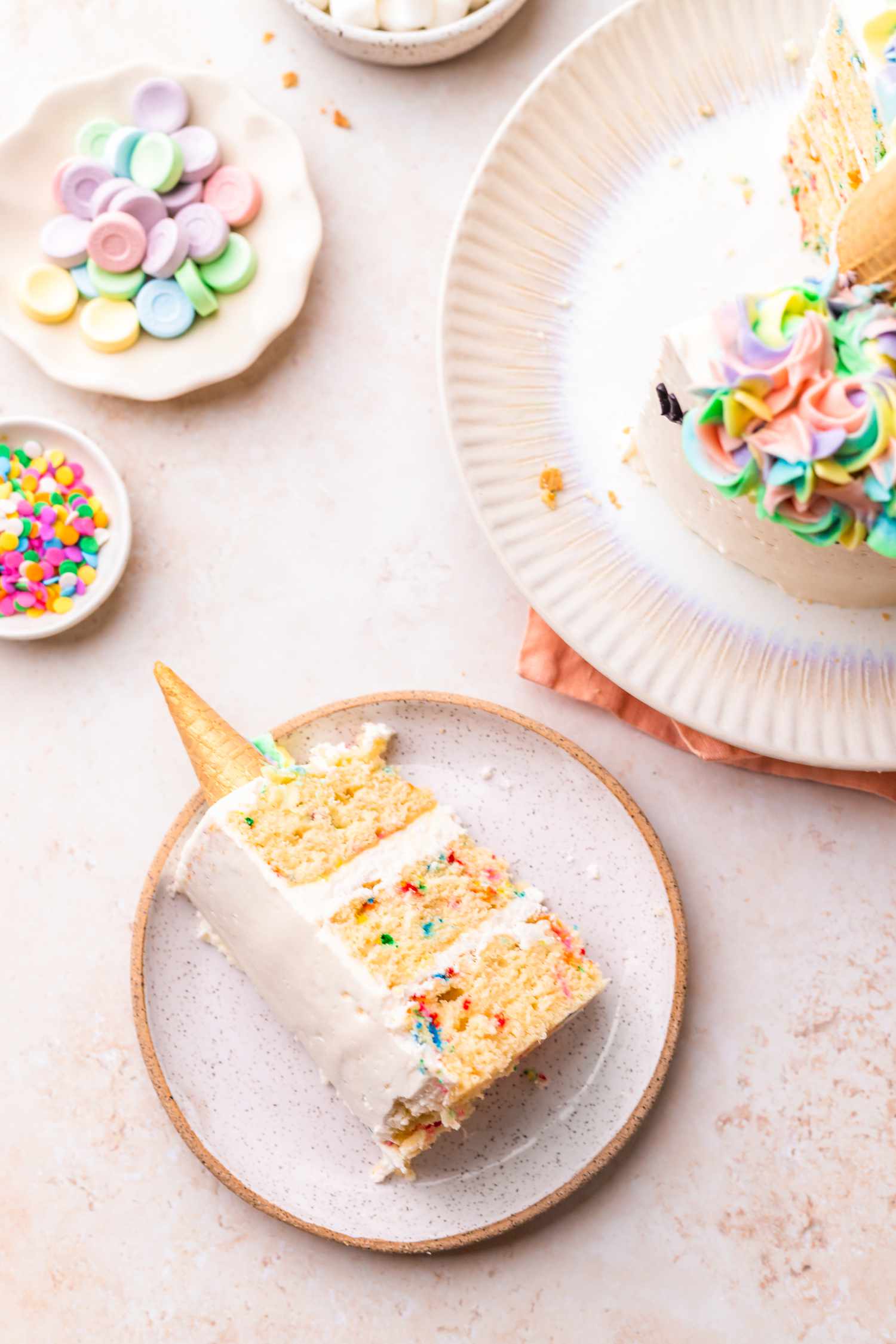 A Slice of Unicorn Cake on a Plate Surrounded by Another Plate with More of the Cake and Smaller Plates with Candies and Sprinkles