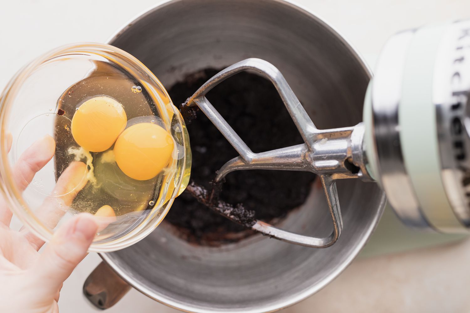Adding eggs to a stand mixer to make chocolate crinkles.