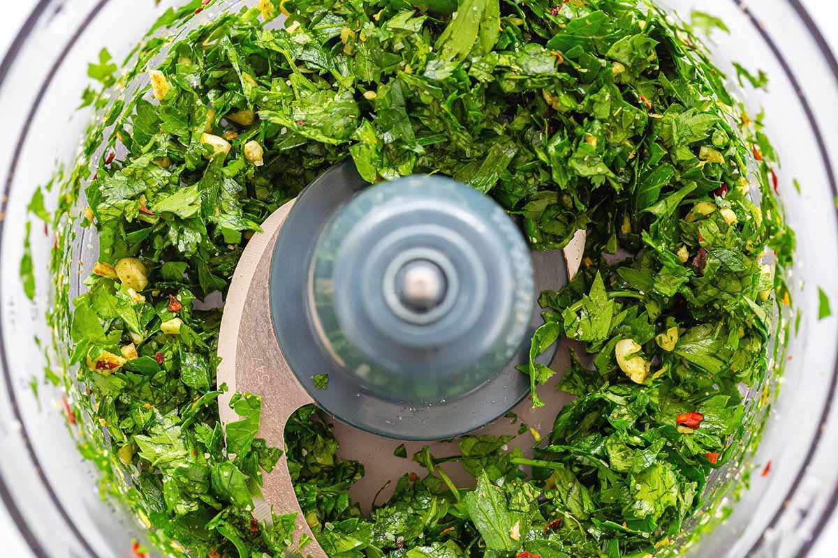 Herbs, spices and oils mixed together in a food processor to make chimichurri with avocados for skirt steak