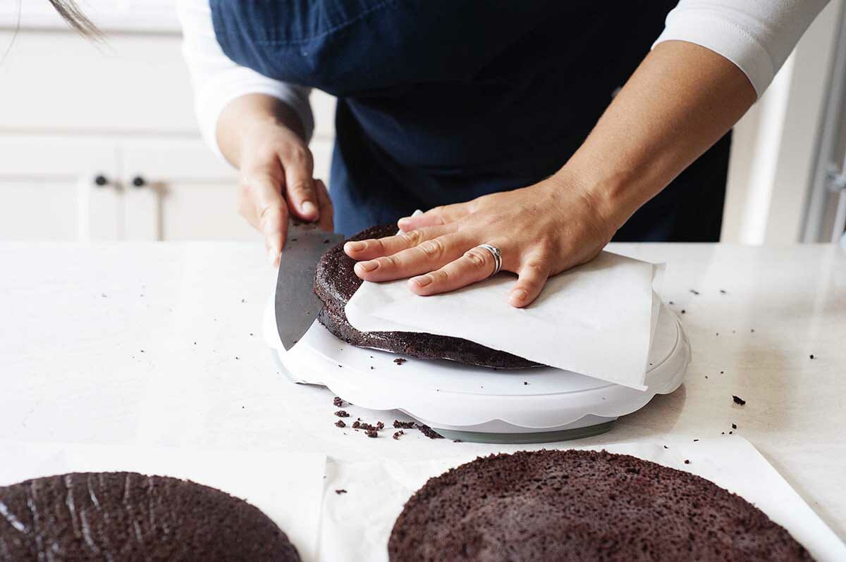 Chocolate cake rounds being cut horizontally to make Cherry Chocolate Cake with Whipped Cream.