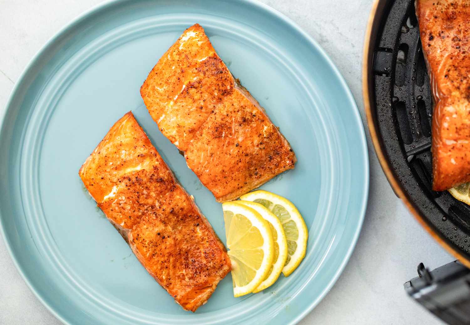 Air Fryer Salmon on a Plate with Lemon Wedges Next to an Air Fryer 