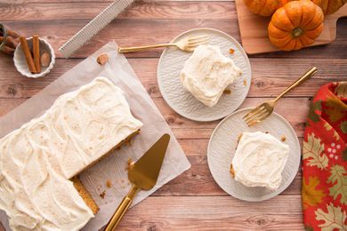 Pumpkin Snack Cake frosted with cream cheese is set on a table with two plates with pieces of cake to the right.