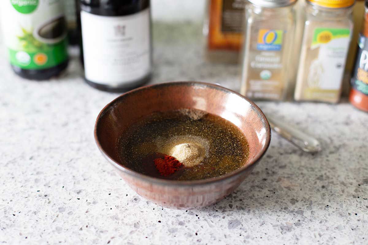 Small bowl with ingredients for easy balsamic marinade. Spices and ingredients are behind the bowl.