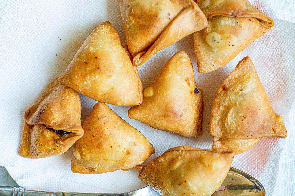 Triangles of the best vegetables samosas drainging on a plate with paper towels.