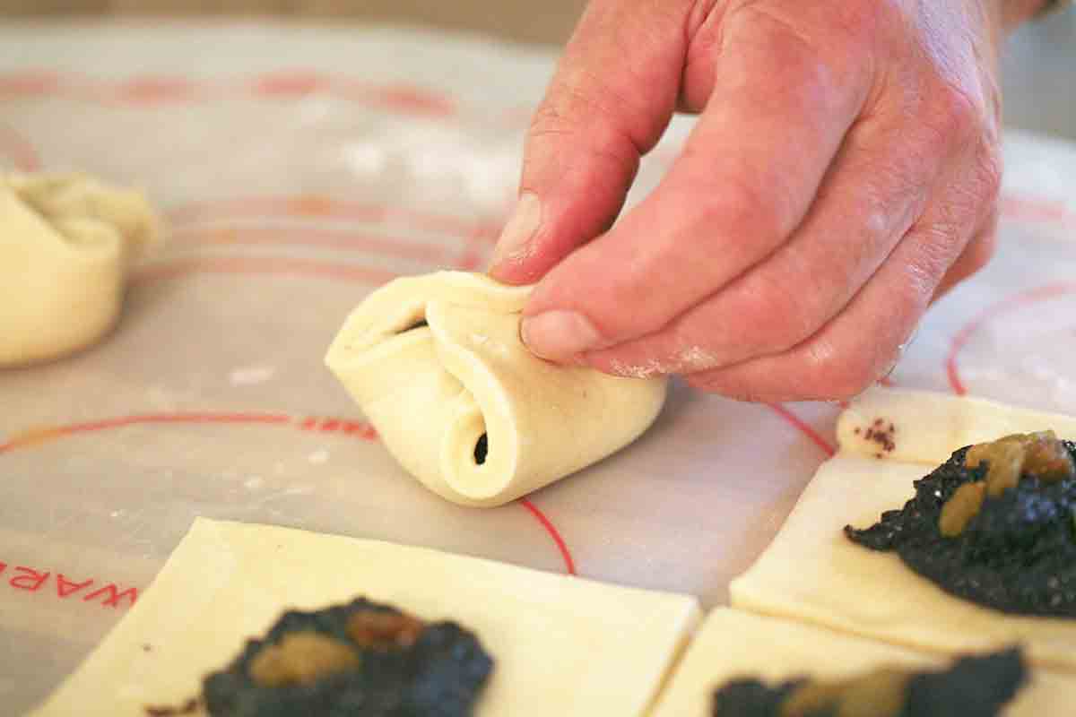 A hand folding poppy seed filling up in kolache dough
