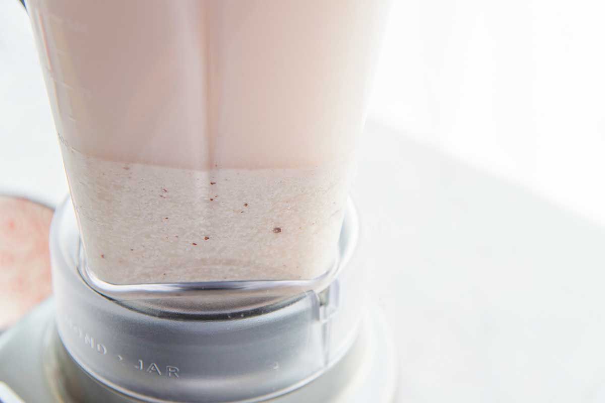 Close up side view of the inside of a blender with rice and creamy liquid inside for homemade horchata.