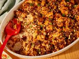 Greek-style stuffing in an oval white serving dish, with a red serving spoon in the right corner where some of the stuffing has been scooped out