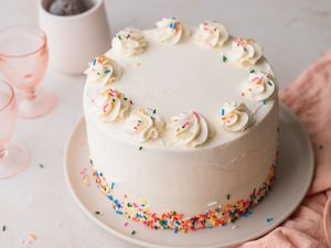 Decorated Rainbow Layer Cake on a Plate with Glasses in Background