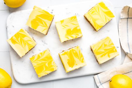 Lemon Cheesecake Bars on a Marble Board, and on the Counter, Lemons and a Kitchen Towel