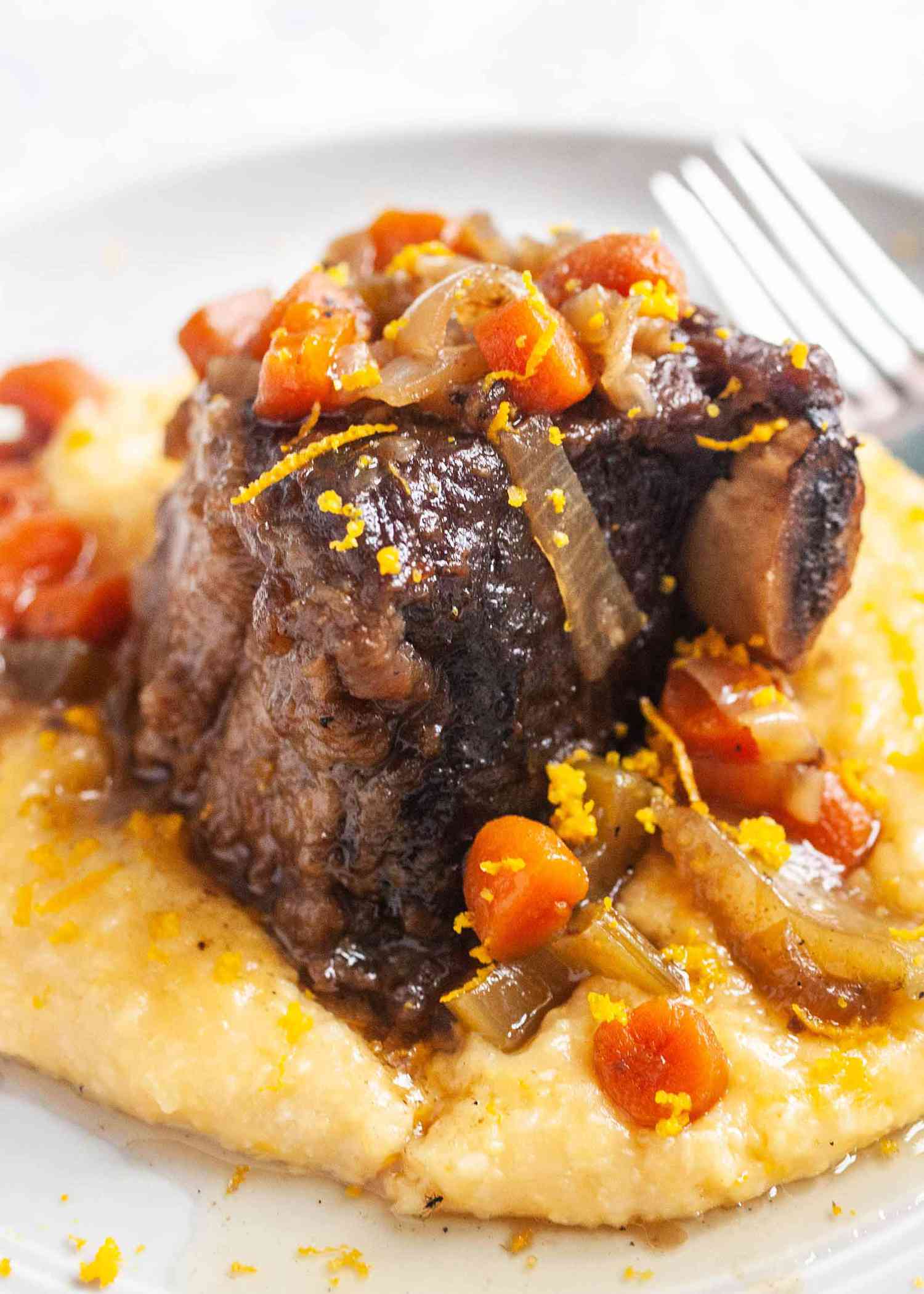 Crockpot Braised Beef Short Ribs with Polenta and carrots on a round plate