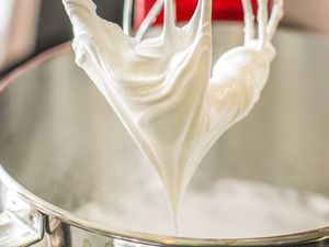 Whipped cream being prepared with a stand mixer, forming peaks in a metal mixing bowl