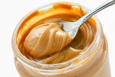 A close up shot of an open jar of peanut butter with a spoon taking out a scoop
