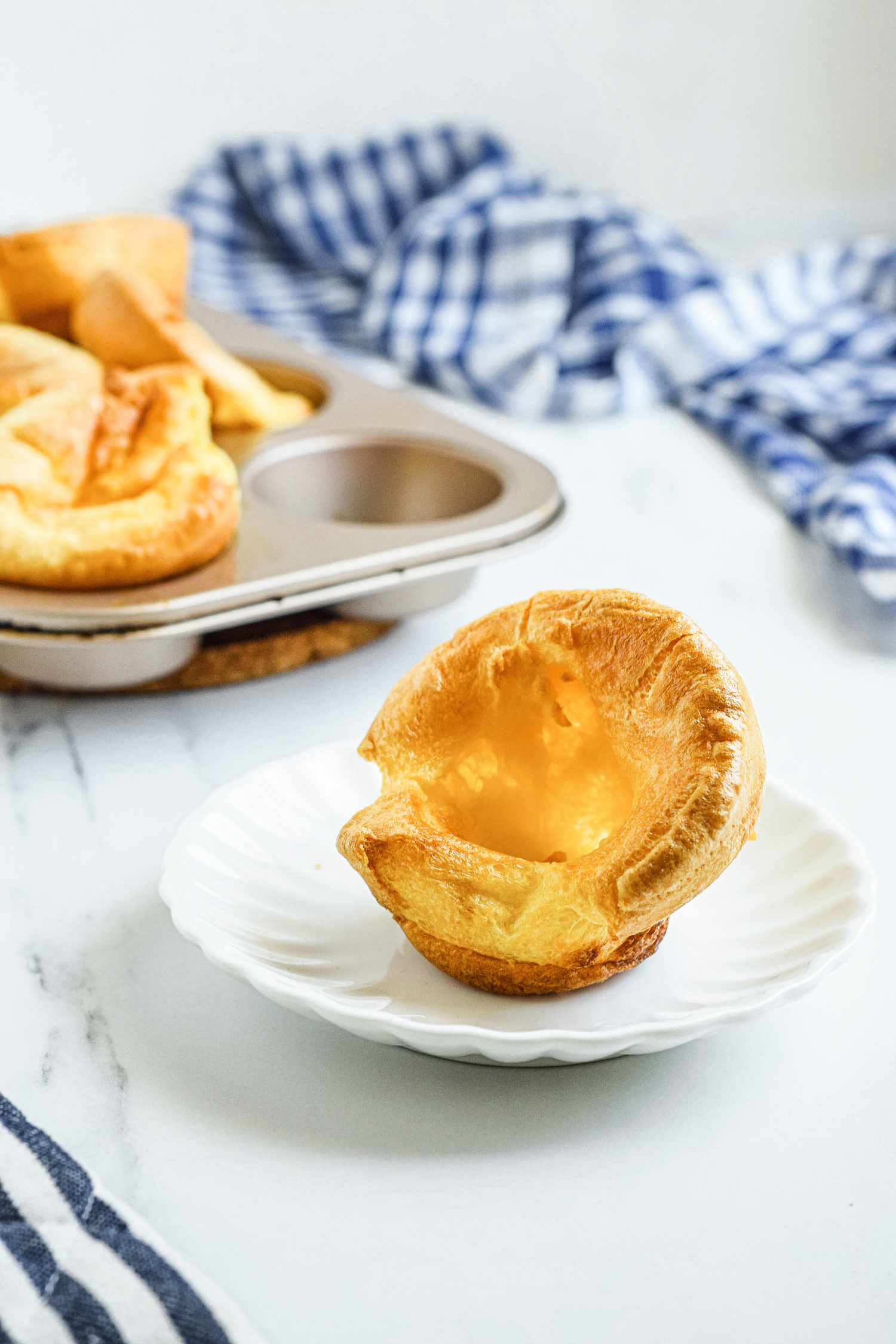 A plate with a yorkshire pudding on it and more in the background along with a striped linen.