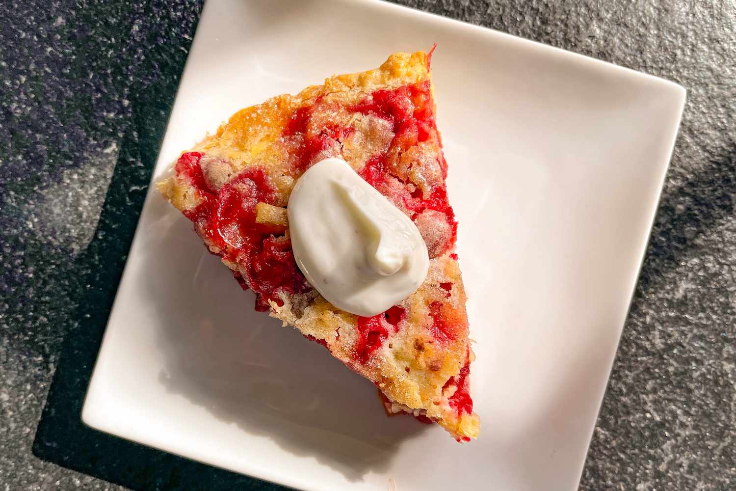A wedge of the cranberry apple cake on a square plate, topped with a dollop of vanilla Greek yogurt