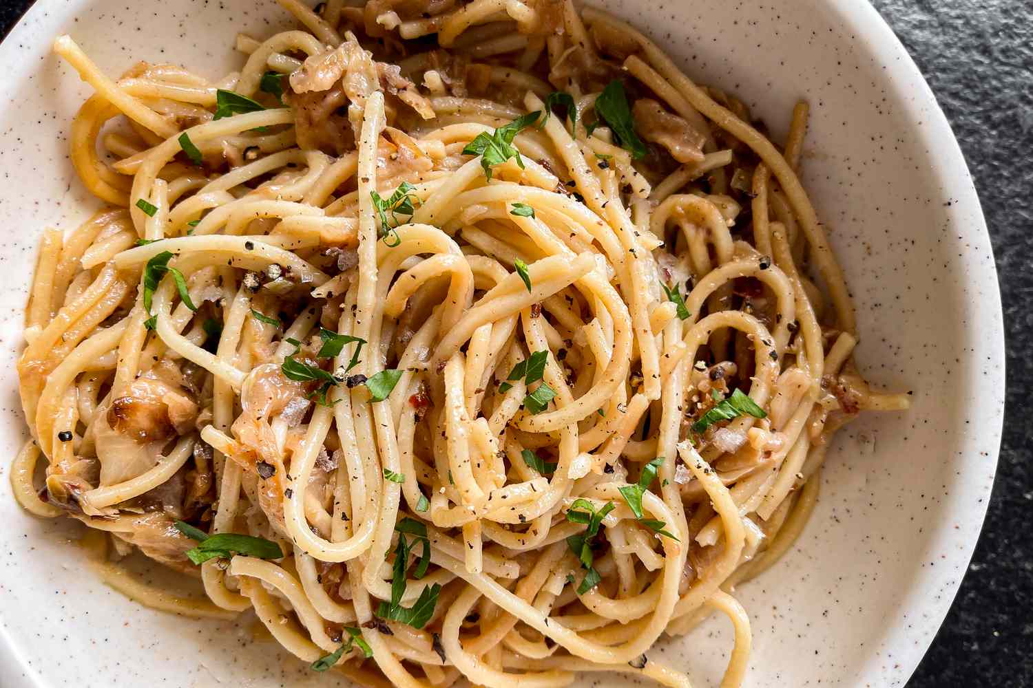 A closeup of caramelized cabbage spaghetti in a white bowl, garnished with parsley