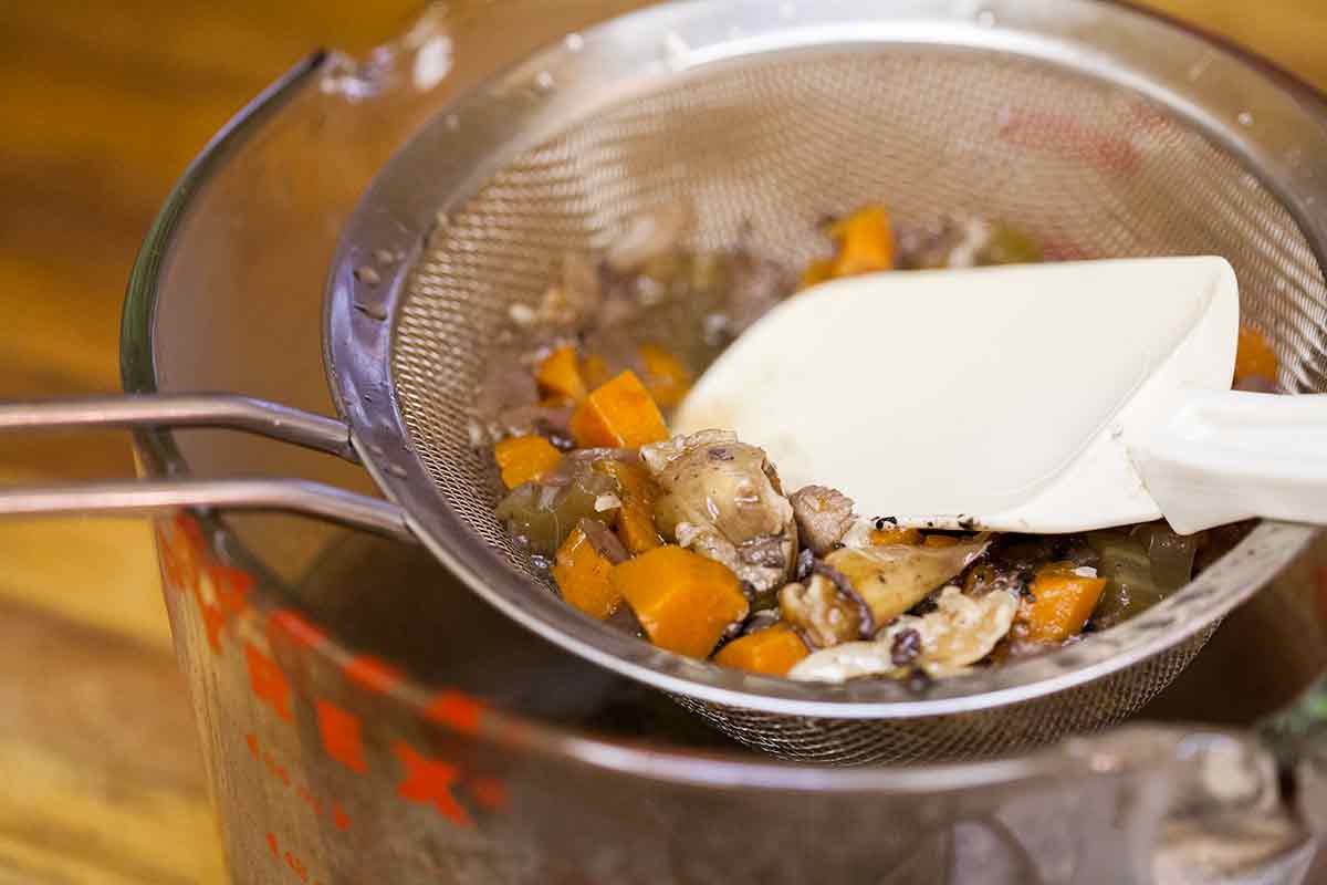 Vegetable liquid being strained through a strainer into a measuring glass