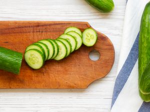 cucumbers sliced on a cutting board next to more (uncut) cucumbers on the counter