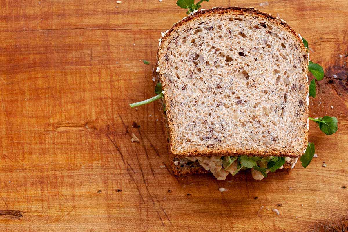 One chickpea salad sandwich on whole grain bread on a cutting board.