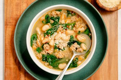 serving of 15-Minute Sausage White Bean Soup in a white bowl on a dark green plate on a wooden serving board
