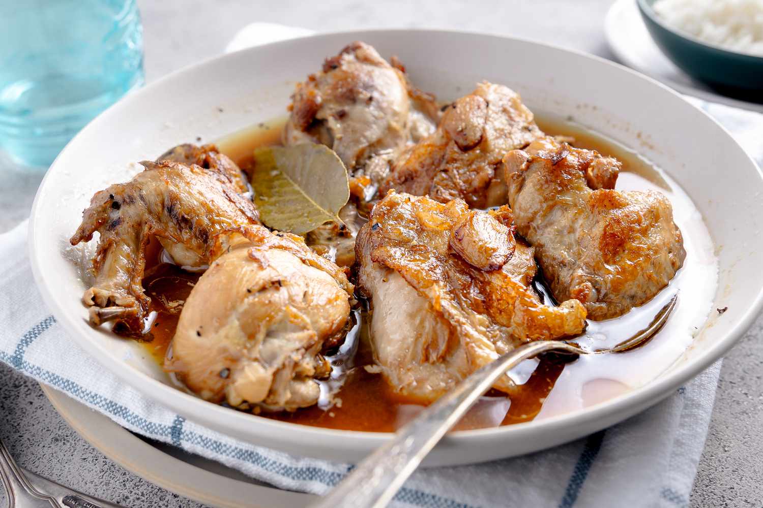 Chicken Adobo in a Bowl With a Spoon, and Under the Bowl, a Kitchen Towel