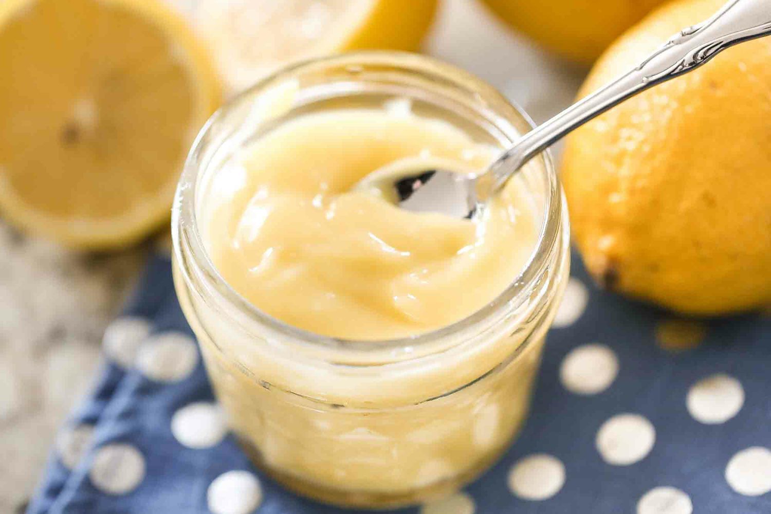 lemon curd in a jar with a spoon and a blue and white polka dot cloth