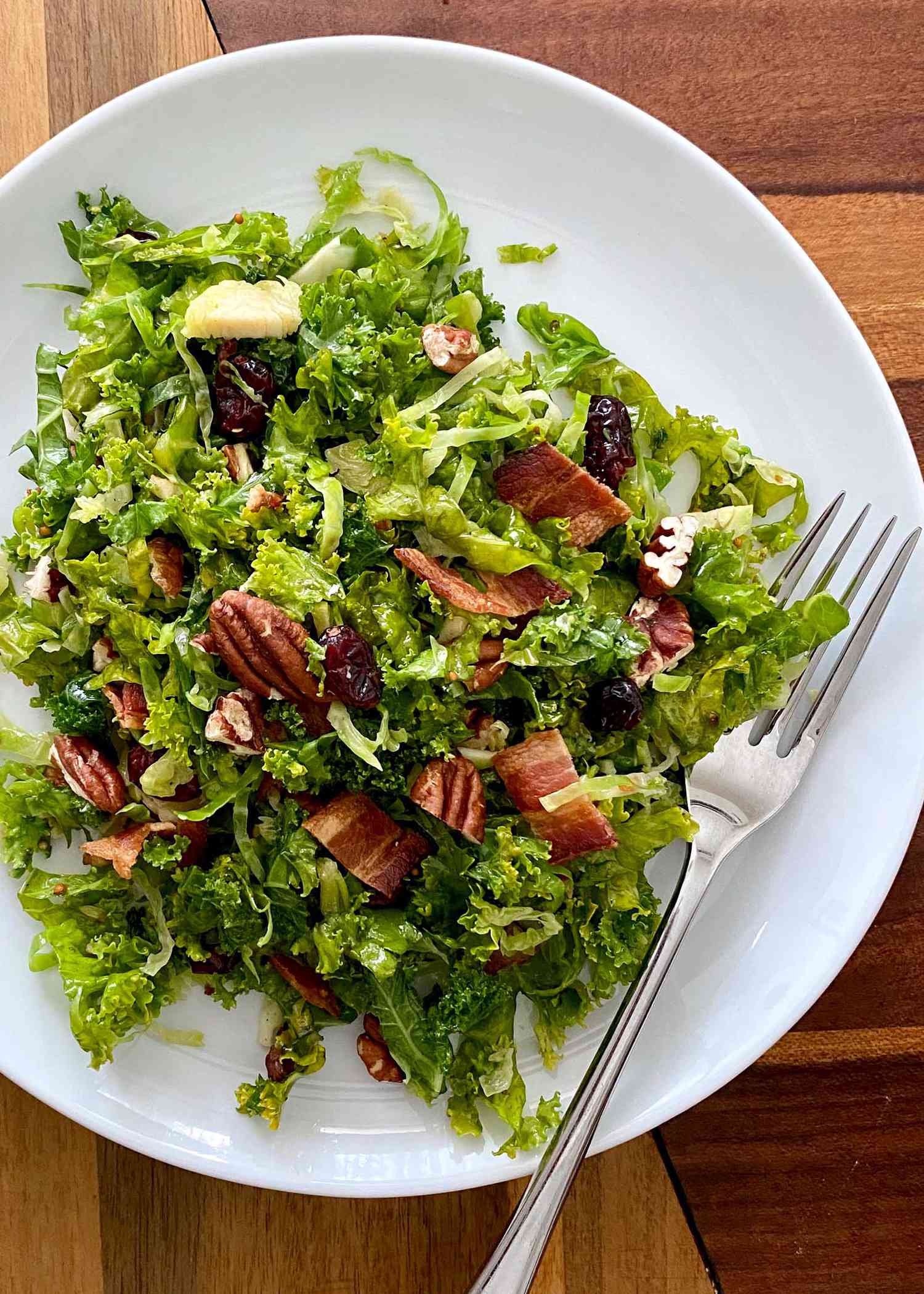 Raw Kale and Shaved Brussels Sprout Salad with Maple Dijon Vinaigrette on a plate with a fork to the right.