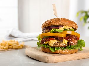 A loaded cheeseburger with vegetables and a bun on a wooden tray