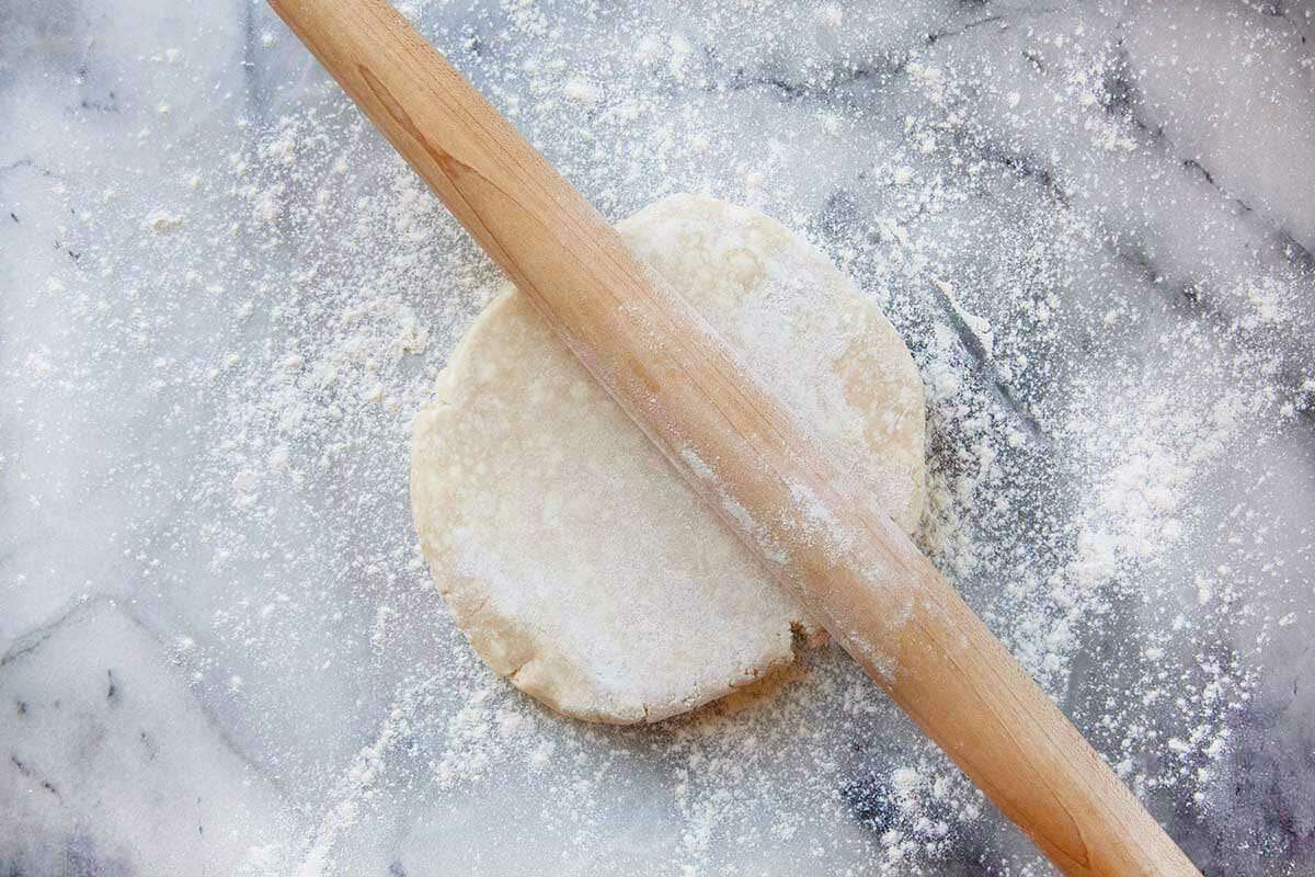 A long thin rolling pin is set on top of a disk of pie dough to make shoo-fly pie.