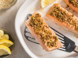4-ingredient mediterranean salmon on a platter next to a bowl of lemon wedges and a glass of wine 