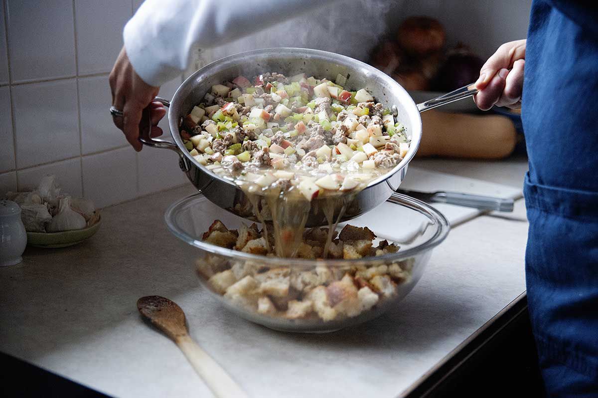 Woman pouring hot liquid inot a bowl of bread to make classic Thanksgiving Stuffing.