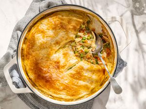 Overhead view of a dutch oven of weeknight chicken pot pie with a serving spoon all resting on a gray kitchen towel on a marble countertop