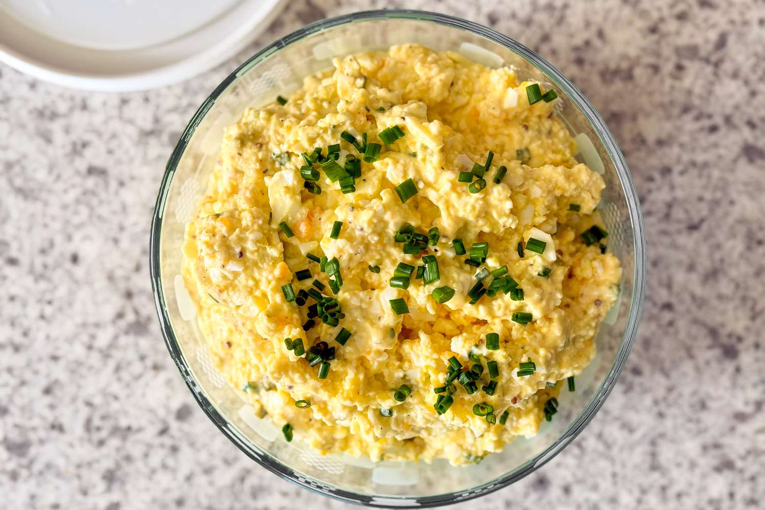 Overhead shot of a clear bowl with egg salad, garnished with chopped chives