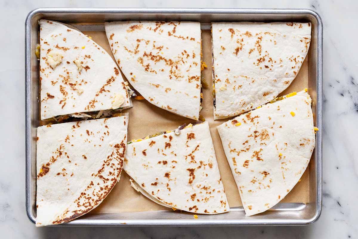 Freezer-friendly breakfast quesadillas cut in triangles and set on a baking sheet covered in parchment. The baking sheet is on a marble background.
