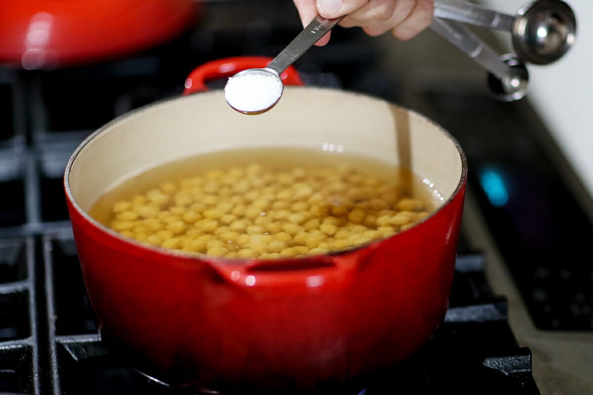 Pot of beans in the stove with a spoonful of salt about to go in