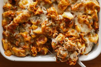 Casserole dish of tortellini casserole, serving spoon removing a cheesy spoonful