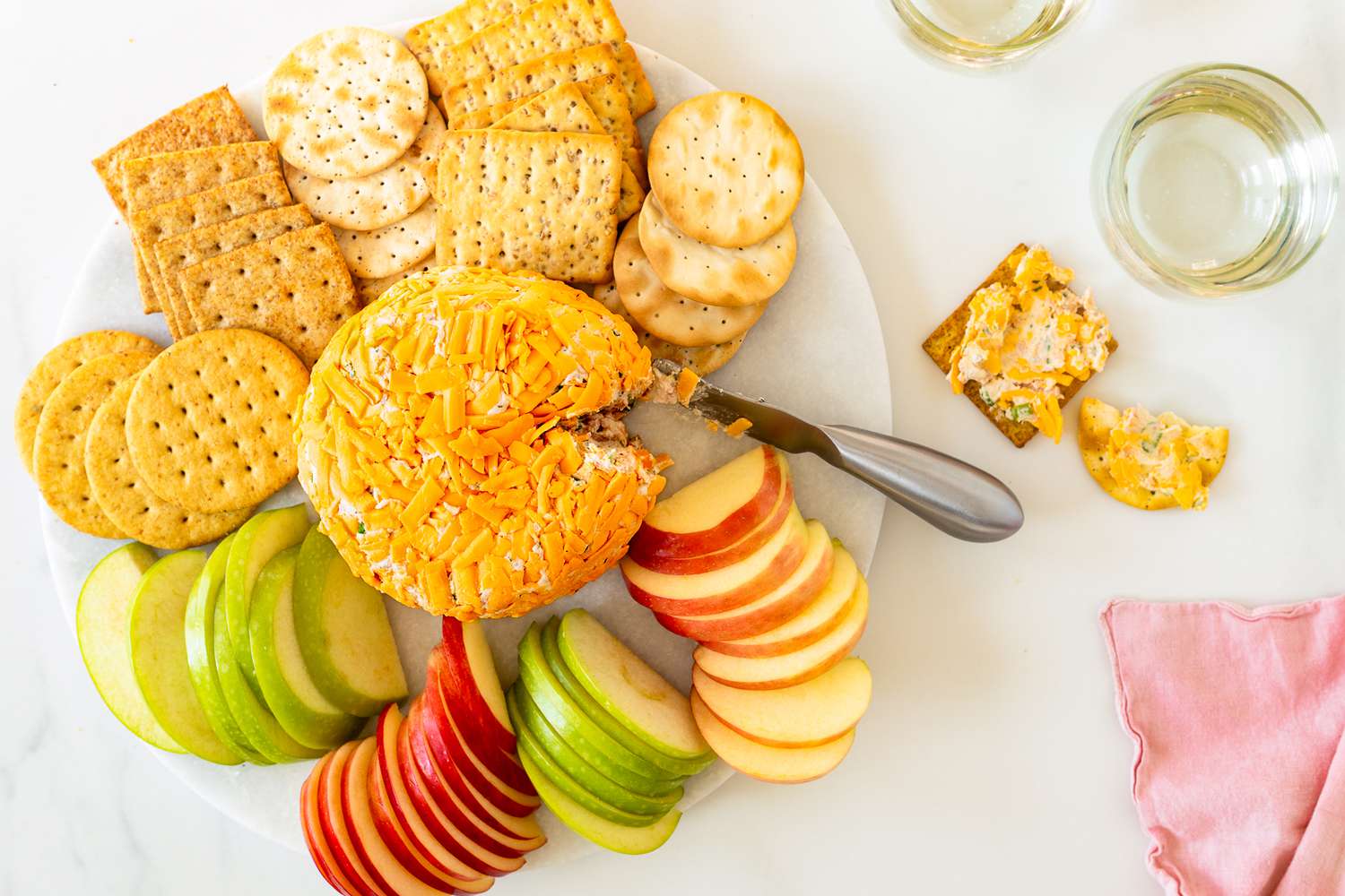 Overhead view of a white plate of a ham ball appetizer surrounded by various crackers and apple slices