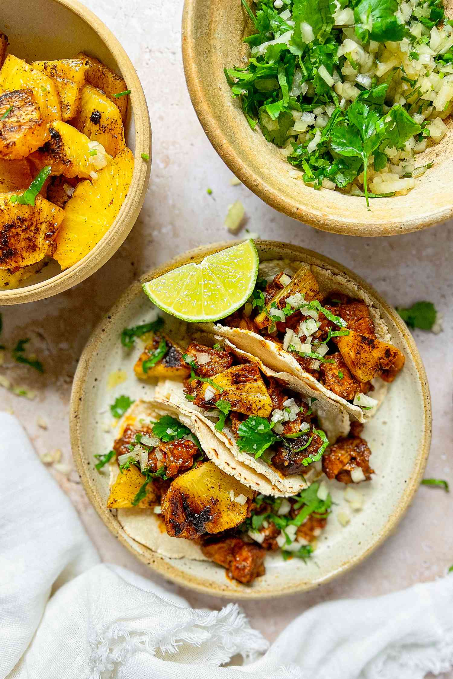 Plate of Tacos al Pastor with Pork, Pineapple, Cilantro, and a Lime Wedge Surrounded by Additional Taco Ingredients