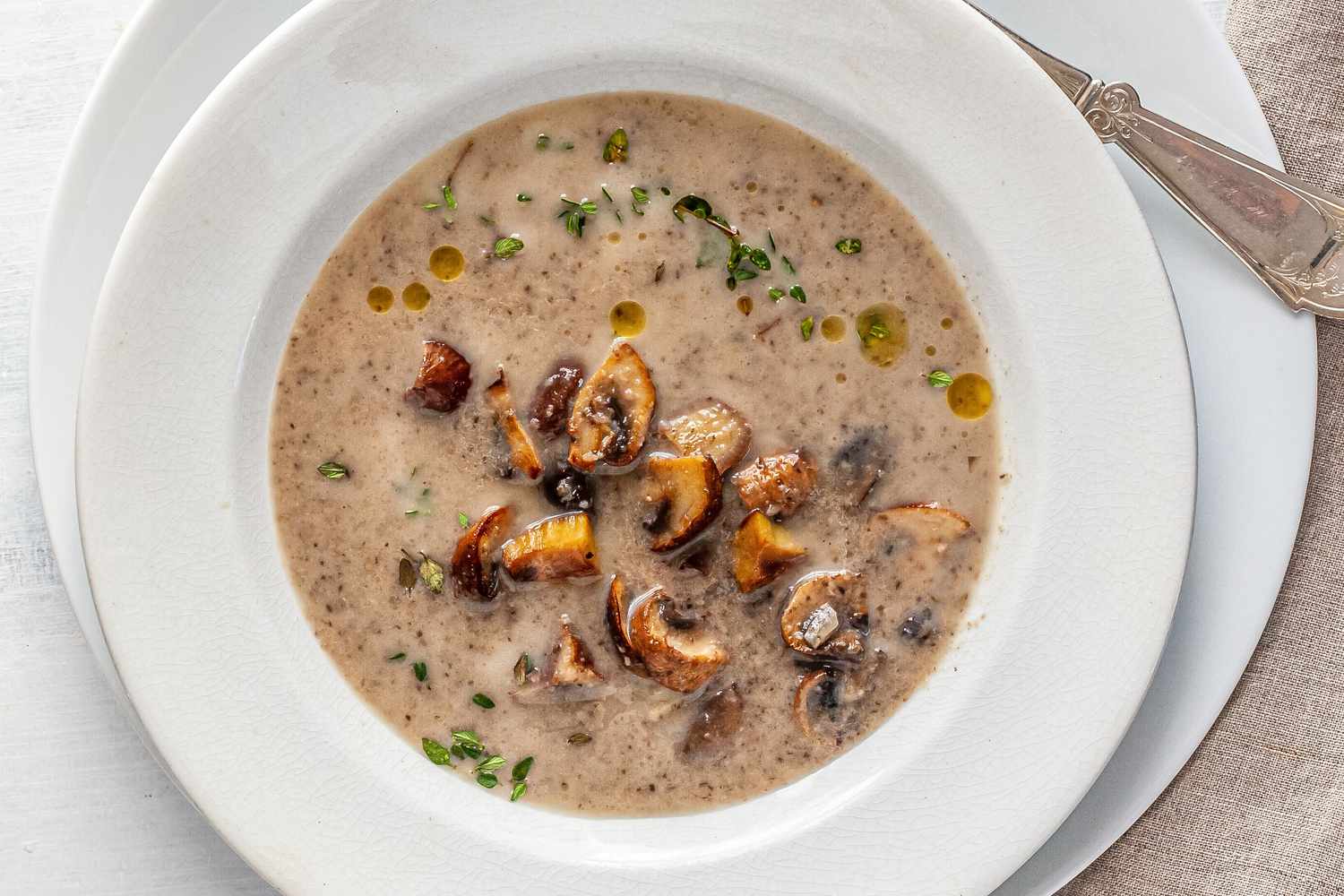 Chestnut mushroom soup in a white bowl with a white plate underneath.