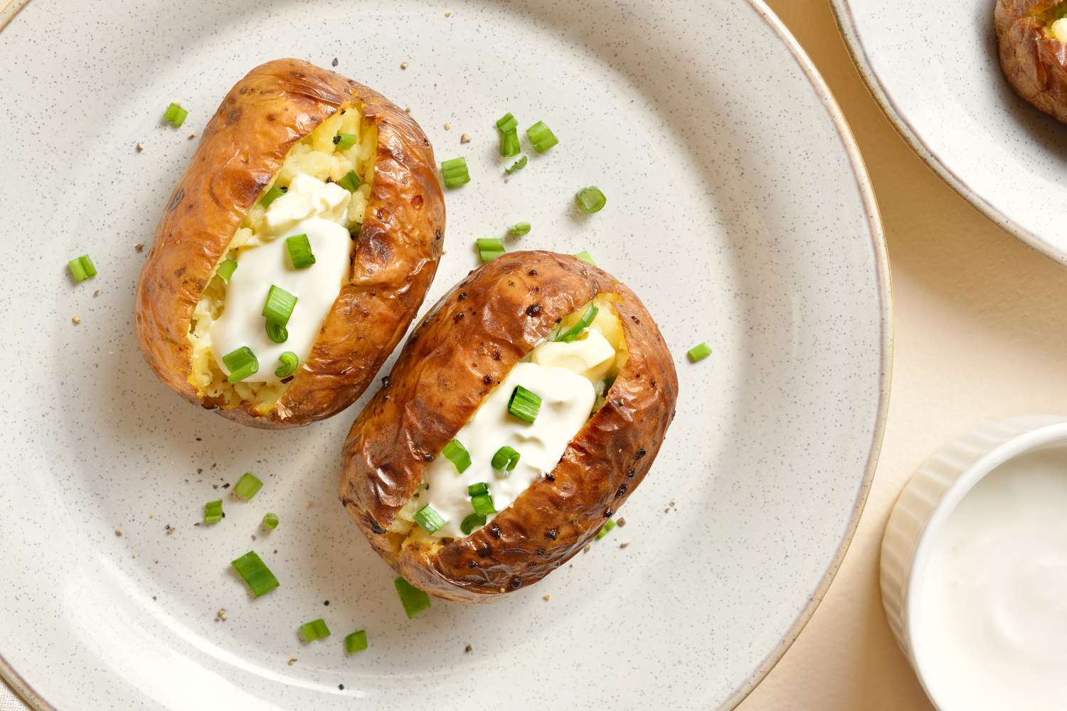 Two baked potatoes on a white plate topped with sour cream and chopped chives